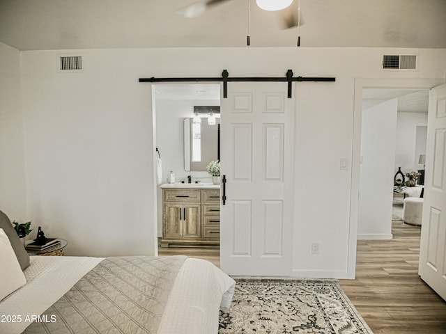 6401 E Eugie Ter, Scottsdale, AZ 85254 - bedroom featuring light wood-style flooring, a barn door, baseboards, connected bathroom, and a sink