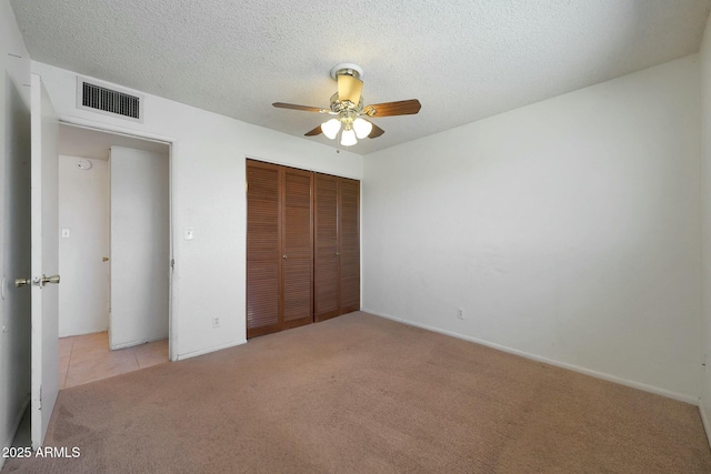 unfurnished bedroom featuring a textured ceiling, a closet, ceiling fan, light carpet, and visible vents