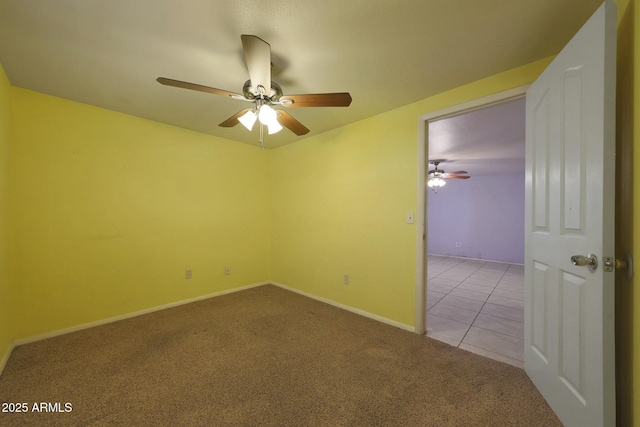 carpeted spare room featuring baseboards, a ceiling fan, and tile patterned flooring