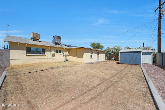 rear view of house featuring central AC unit, fence, a storage shed, an outbuilding, and brick siding