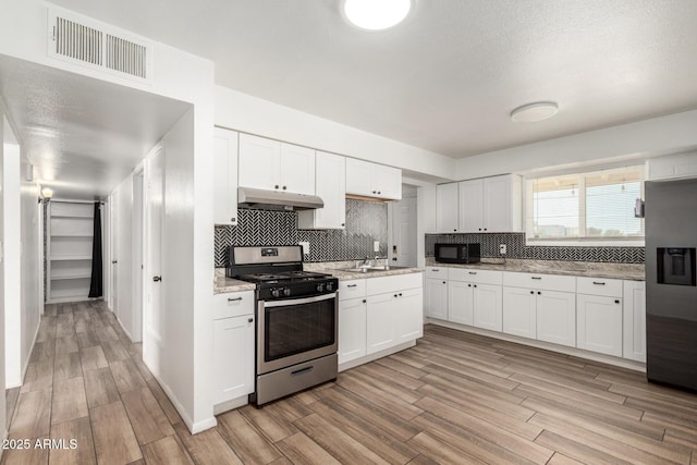 kitchen featuring appliances with stainless steel finishes, under cabinet range hood, light wood-type flooring, and visible vents