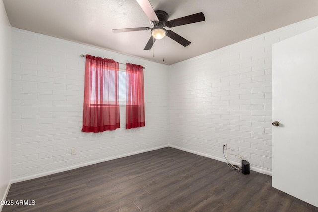 empty room with baseboards, dark wood-style flooring, ceiling fan, and brick wall