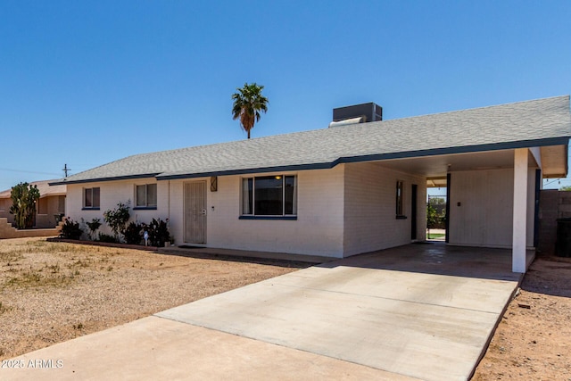 ranch-style home with brick siding, a shingled roof, a carport, and concrete driveway