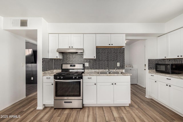 kitchen featuring washer / clothes dryer, gas range, black microwave, light wood-style floors, and under cabinet range hood