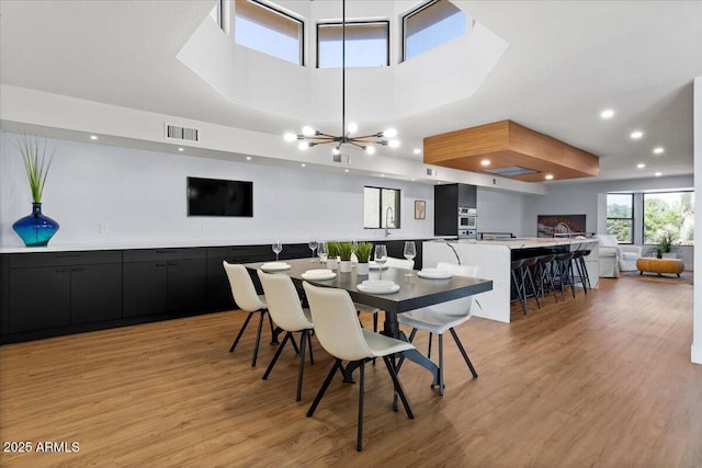 dining space featuring a towering ceiling, light hardwood / wood-style flooring, and a notable chandelier