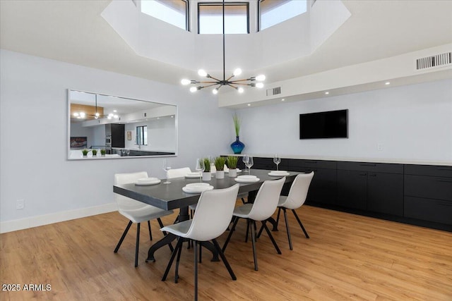 dining room featuring a notable chandelier, light wood-type flooring, and a high ceiling