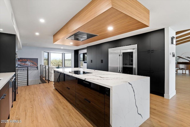 kitchen with a large island, stainless steel built in fridge, black electric cooktop, and light hardwood / wood-style flooring