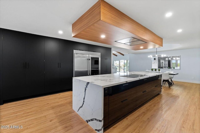 kitchen with a large island, hanging light fixtures, built in fridge, light hardwood / wood-style flooring, and black electric stovetop