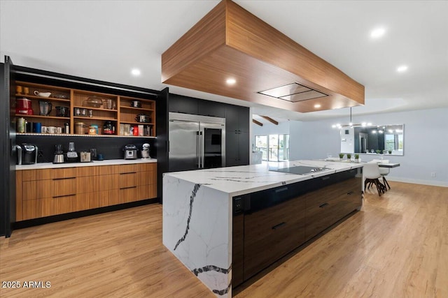 kitchen featuring electric cooktop, light hardwood / wood-style flooring, built in refrigerator, light stone countertops, and a large island