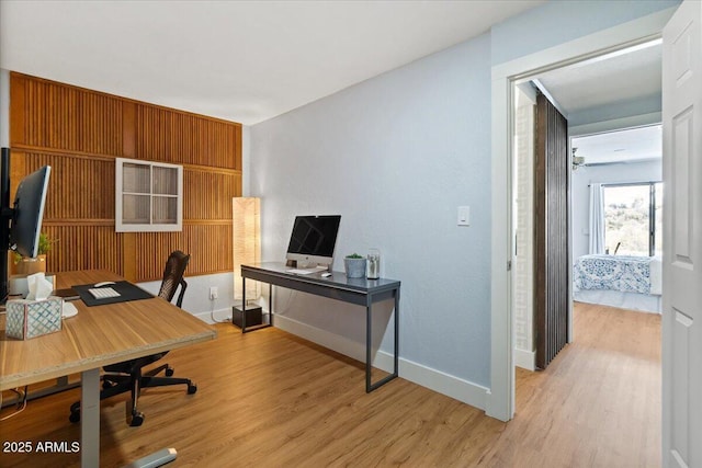 office space with light wood-type flooring, ceiling fan, and wooden walls