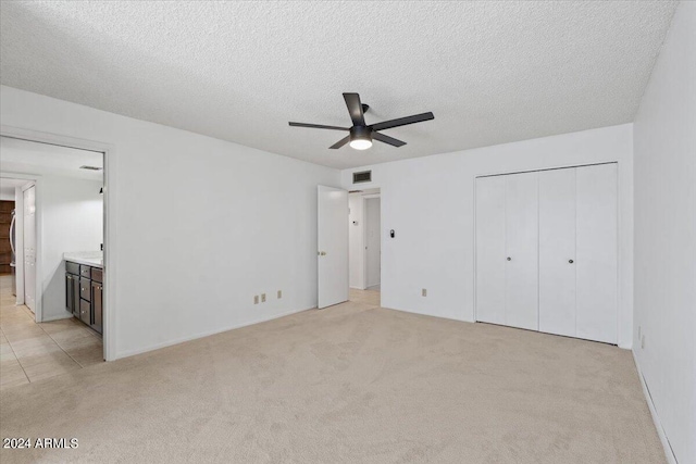 unfurnished bedroom featuring connected bathroom, a closet, light carpet, a textured ceiling, and ceiling fan