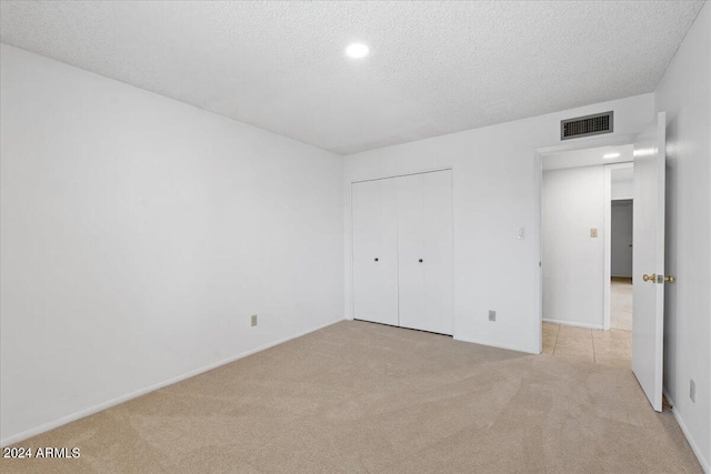 unfurnished bedroom featuring light carpet, a textured ceiling, and a closet