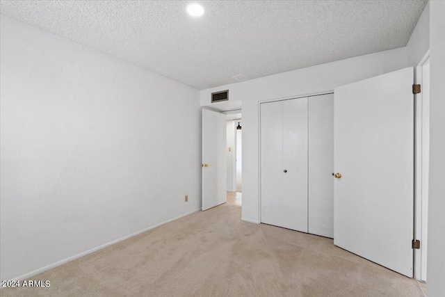 unfurnished bedroom with a closet, light carpet, and a textured ceiling