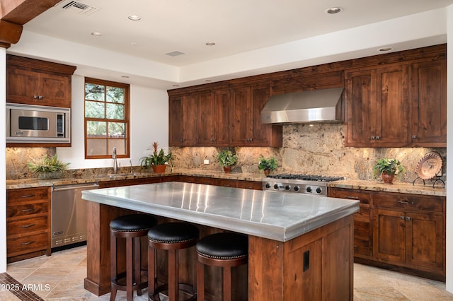 kitchen with visible vents, wall chimney exhaust hood, appliances with stainless steel finishes, a center island, and a sink