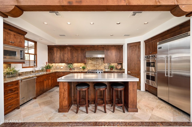 kitchen featuring built in appliances, a center island, visible vents, decorative backsplash, and wall chimney exhaust hood