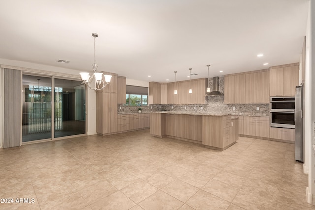 kitchen with light brown cabinets, wall chimney exhaust hood, hanging light fixtures, light stone counters, and a notable chandelier