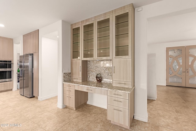 kitchen with appliances with stainless steel finishes, tasteful backsplash, light stone counters, light brown cabinets, and light tile patterned floors