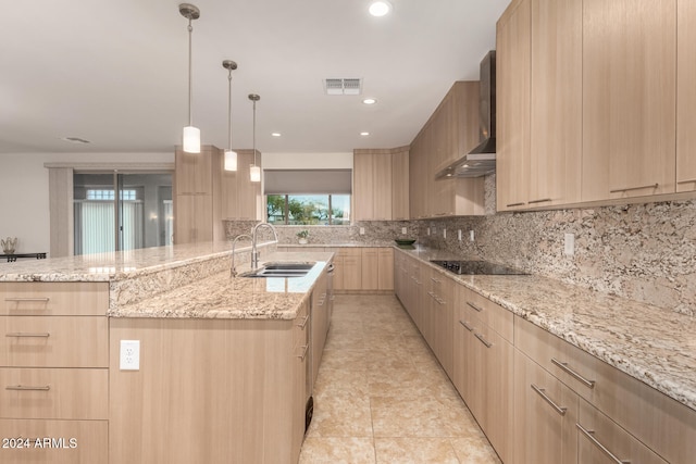 kitchen with light brown cabinets, light stone counters, wall chimney range hood, and sink