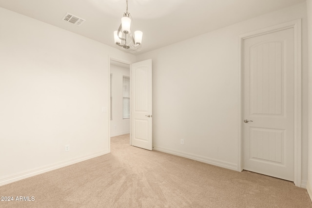 unfurnished room featuring light carpet and a chandelier