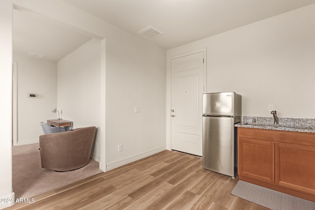 kitchen with stainless steel fridge, light stone countertops, sink, and light hardwood / wood-style flooring