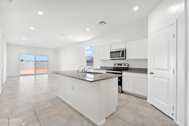 kitchen with a center island with sink, stainless steel appliances, white cabinetry, sink, and dark stone countertops