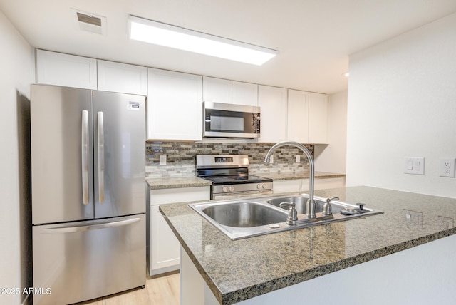 kitchen with decorative backsplash, white cabinets, dark stone countertops, sink, and stainless steel appliances