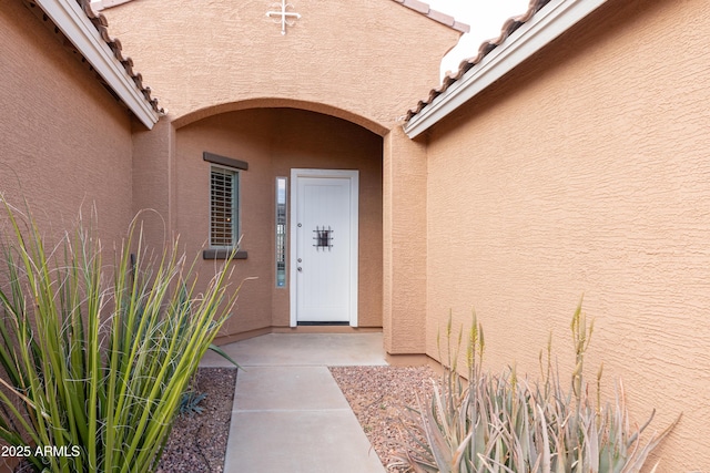 view of exterior entry with stucco siding and a tiled roof