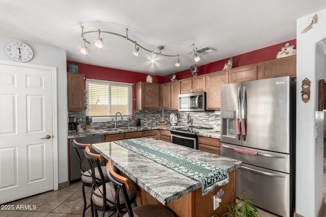 kitchen with a sink, appliances with stainless steel finishes, a center island, tasteful backsplash, and brown cabinetry