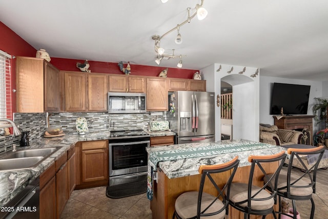 kitchen featuring decorative backsplash, open floor plan, a kitchen breakfast bar, stainless steel appliances, and a sink