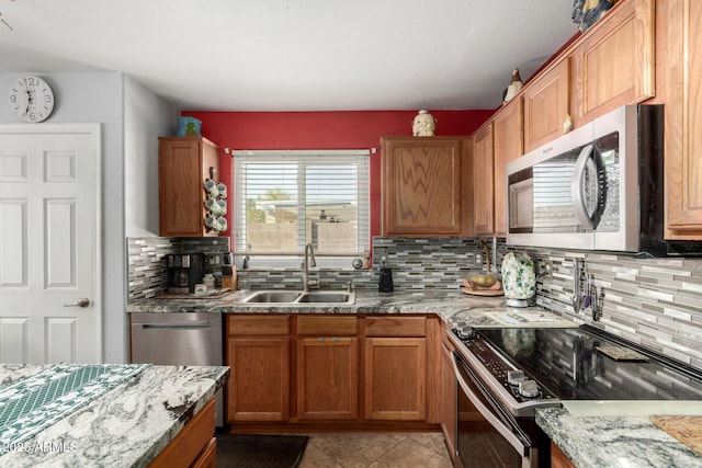 kitchen featuring stainless steel appliances, light stone counters, a sink, and brown cabinets