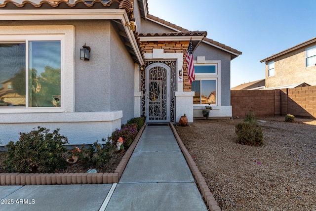 doorway to property with a tile roof, fence, and stucco siding