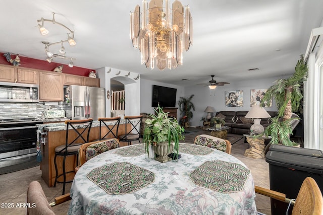 dining space featuring ceiling fan with notable chandelier, arched walkways, and tile patterned floors