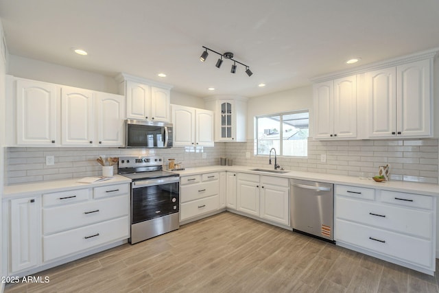 kitchen with tasteful backsplash, white cabinets, stainless steel appliances, light wood-style floors, and a sink