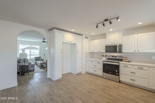 kitchen featuring light wood-style floors, tasteful backsplash, appliances with stainless steel finishes, and arched walkways