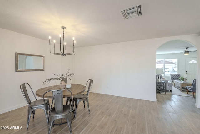 dining area featuring light wood-type flooring, arched walkways, visible vents, and baseboards