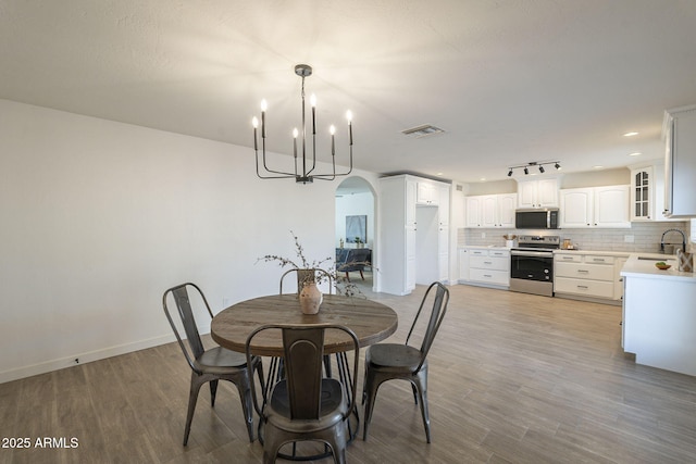 dining area with arched walkways, a chandelier, visible vents, and light wood-style floors