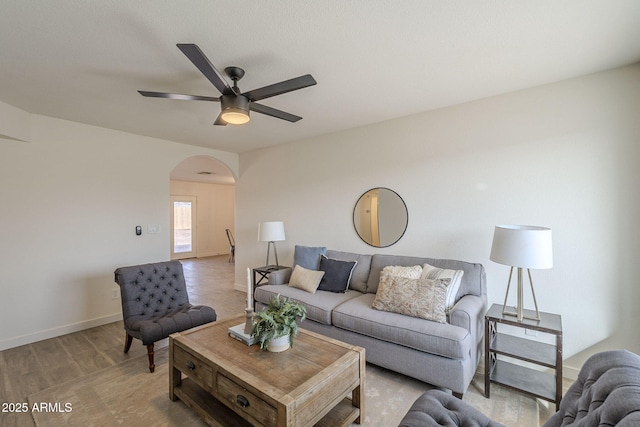 living area with baseboards, arched walkways, and ceiling fan