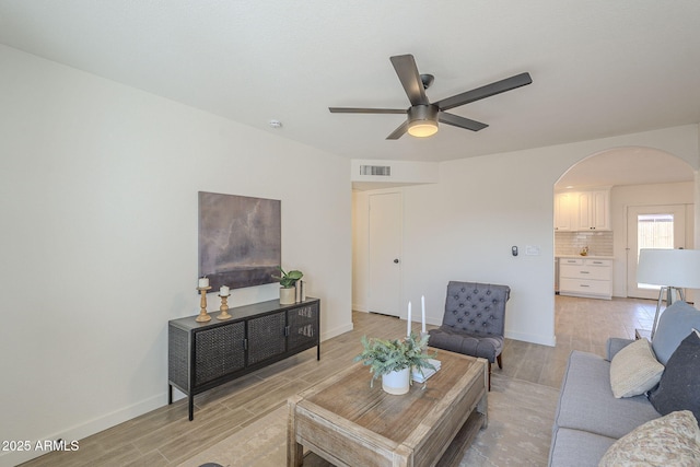 living room featuring arched walkways, light wood finished floors, visible vents, a ceiling fan, and baseboards