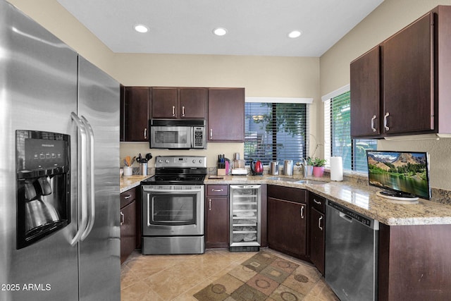 kitchen with sink, appliances with stainless steel finishes, wine cooler, light stone counters, and dark brown cabinetry