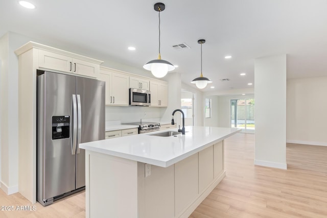 kitchen featuring stainless steel appliances, a sink, light countertops, light wood-type flooring, and a center island with sink