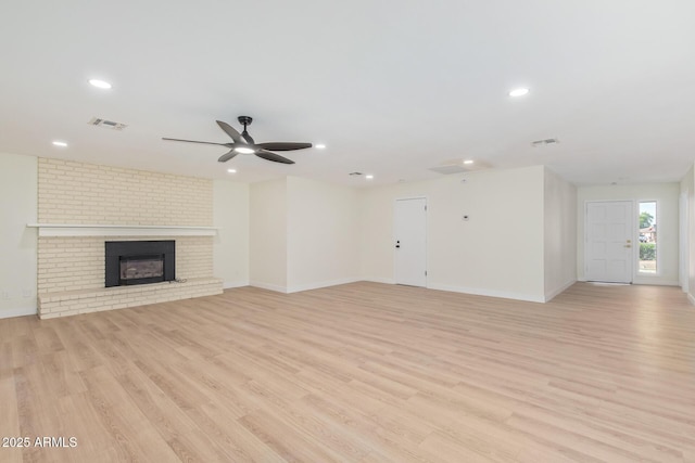 unfurnished living room with light wood-type flooring, a brick fireplace, and visible vents