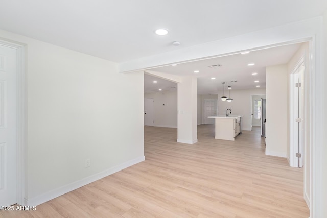 empty room with light wood-type flooring, a sink, baseboards, and recessed lighting