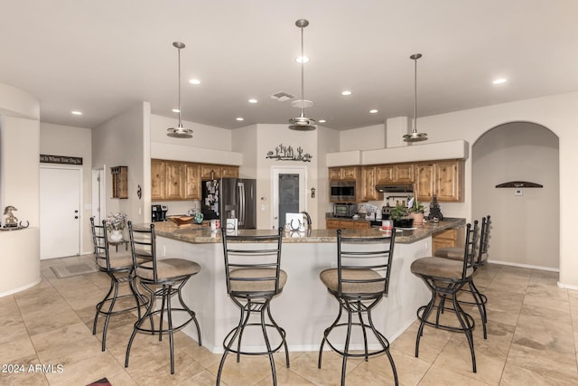 kitchen featuring visible vents, arched walkways, a breakfast bar area, brown cabinets, and stainless steel appliances