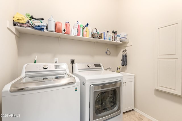 clothes washing area featuring light tile patterned floors, washing machine and dryer, cabinet space, and baseboards