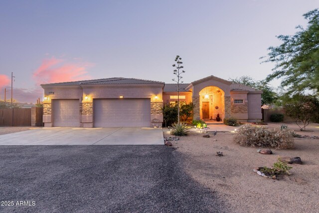 view of front of home with an attached garage, fence, stone siding, concrete driveway, and a tiled roof