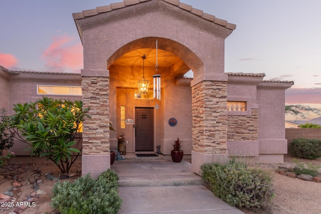 exterior entry at dusk featuring stone siding, a tiled roof, and stucco siding