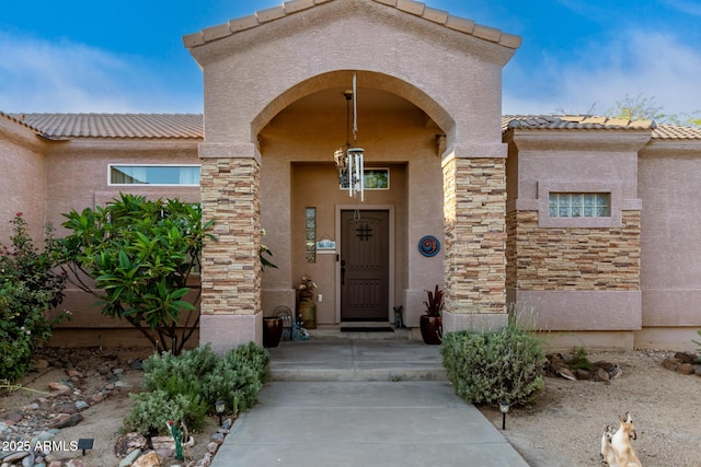 property entrance featuring a tiled roof, stone siding, and stucco siding