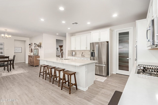 kitchen featuring sink, a breakfast bar, stainless steel appliances, white cabinets, and a center island with sink