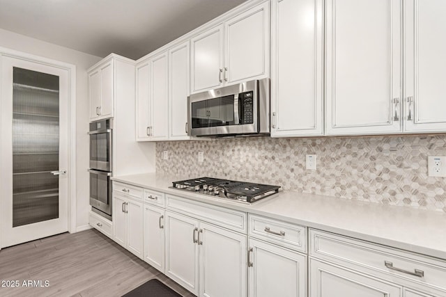 kitchen with stainless steel appliances, white cabinetry, backsplash, and light hardwood / wood-style flooring