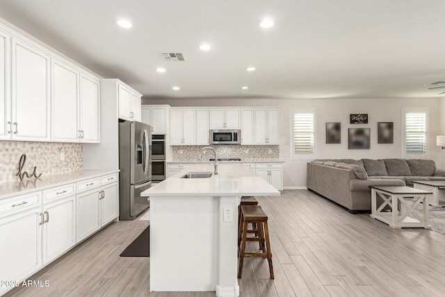 kitchen featuring appliances with stainless steel finishes, a kitchen island with sink, sink, and white cabinets